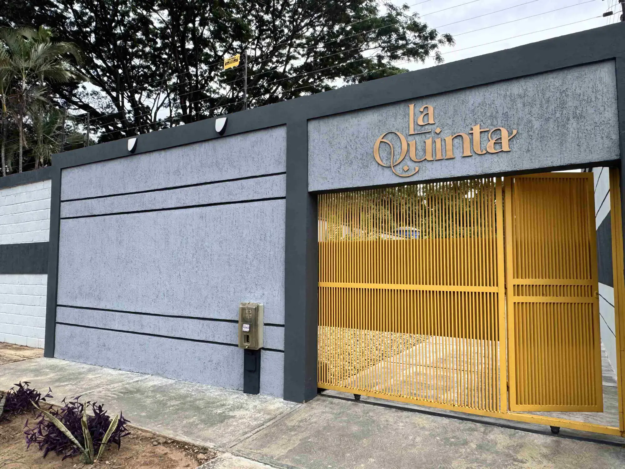 Fachada de La Quinta Showroom: el logotipo dorado sobre el muro y el portón de acceso